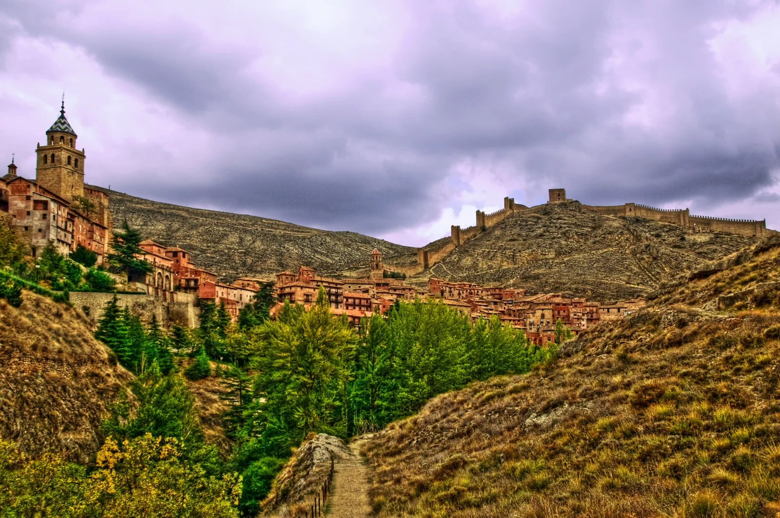 Albarracín's houses and church towers above a green ravine, with defensive walls on the hillside.