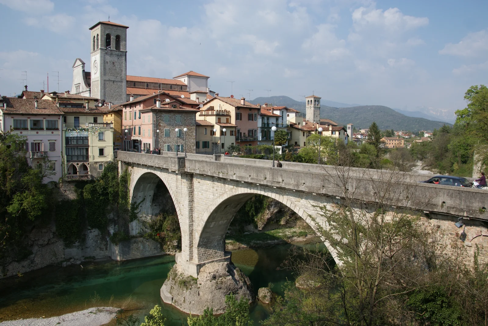 The two stone arches of the Ponte del Diavolo cross the Natisone beneath Cividale’s cathedral tower and colorful houses.
