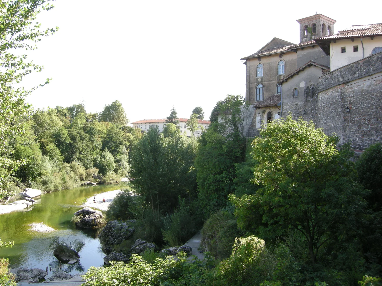 Green water and riverside trees beneath the stone walls of Santa Maria in Valle and the Tempietto complex.