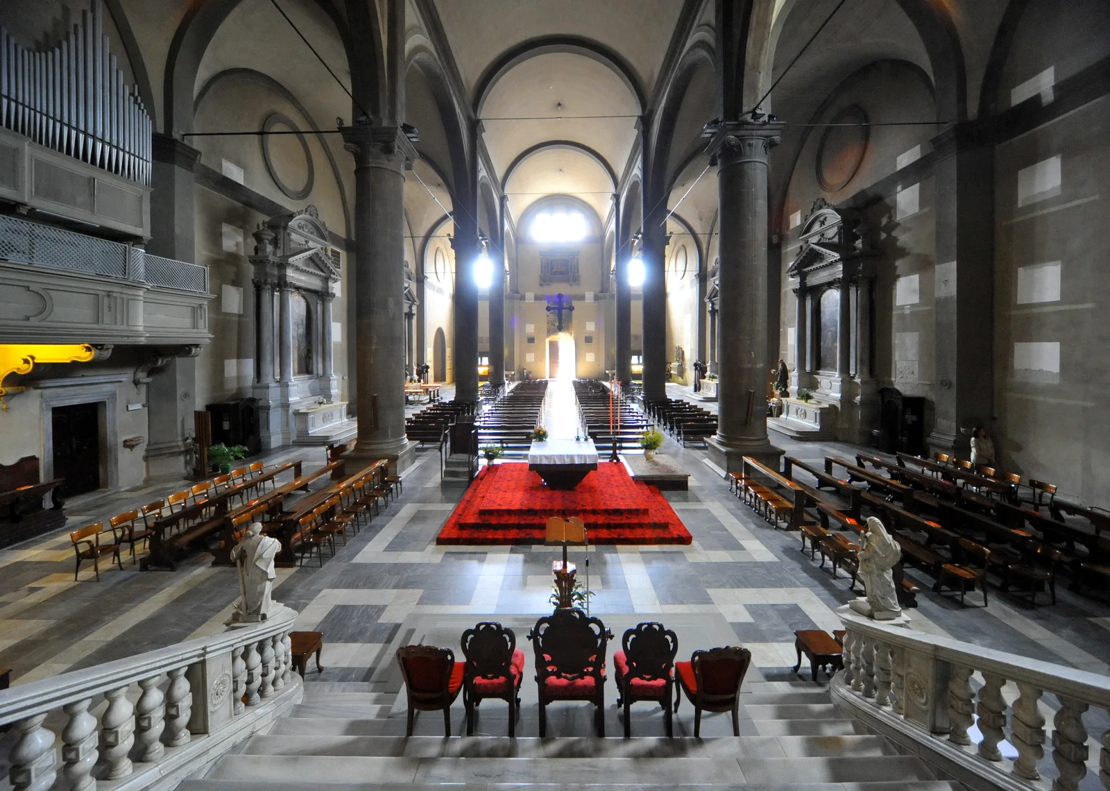 Tall arches and rows of wooden pews lead toward the illuminated altar in Cividale’s cathedral interior.
