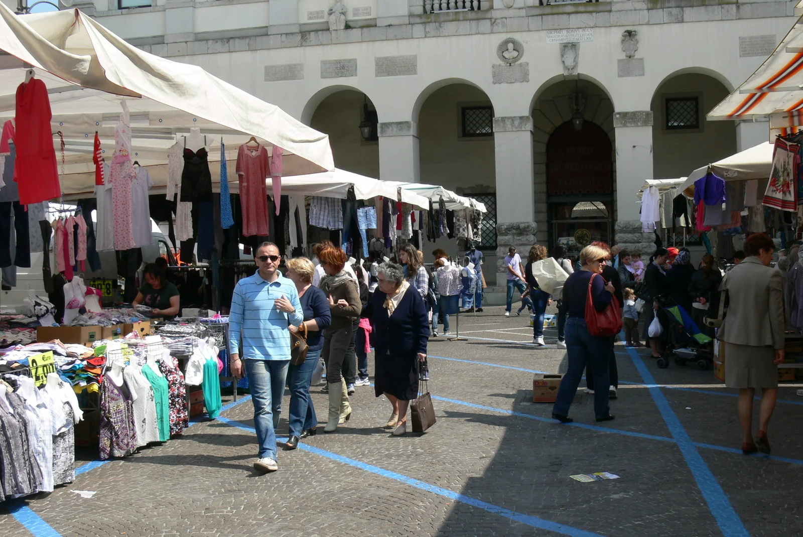 Shoppers pass fabric stalls beneath pale arcaded buildings at a market in Piazza Duomo in April 2011.