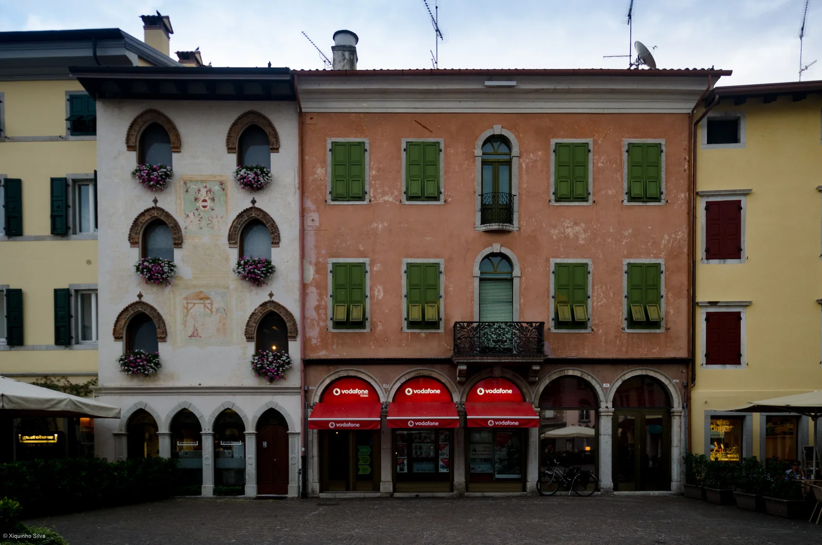 Pastel facades with green shutters, arched ground-floor openings and cafe awnings in Cividale’s town center.