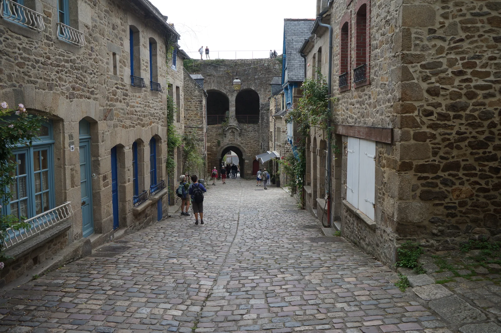 A cobbled street between stone houses descends toward Dinan's arched Jerzual gate.