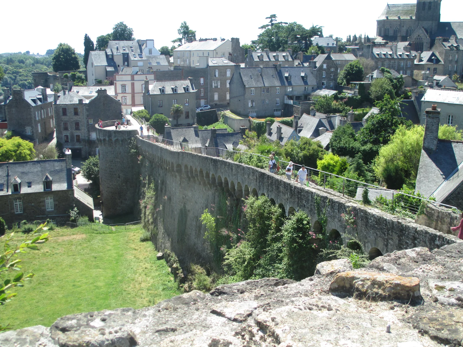 Visitors on Dinan's stone ramparts above a grassy slope, houses and a church.