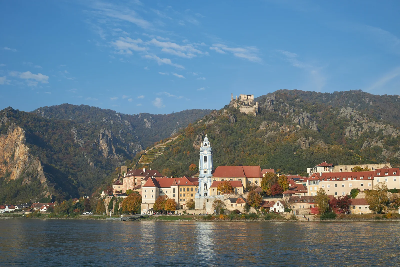 Dürnstein beside the Danube, with the blue abbey tower, red roofs, vineyard terraces and castle ruins on an autumn hillside.