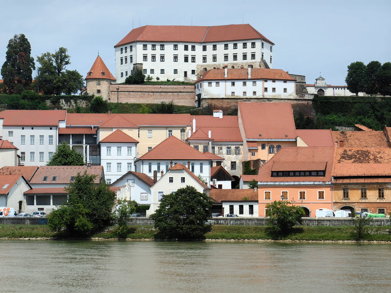 Ptuj Castle above red-roofed buildings beside the Drava River.