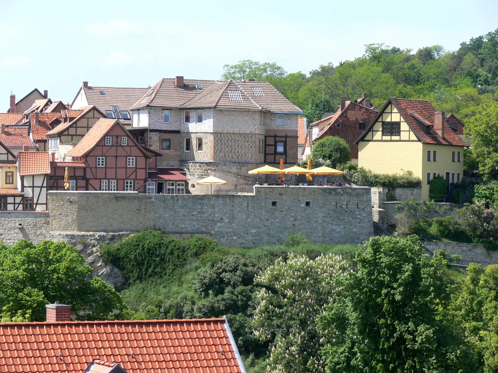 Small timber houses on the Münzenberg stand above a stone retaining wall and green hillside.
