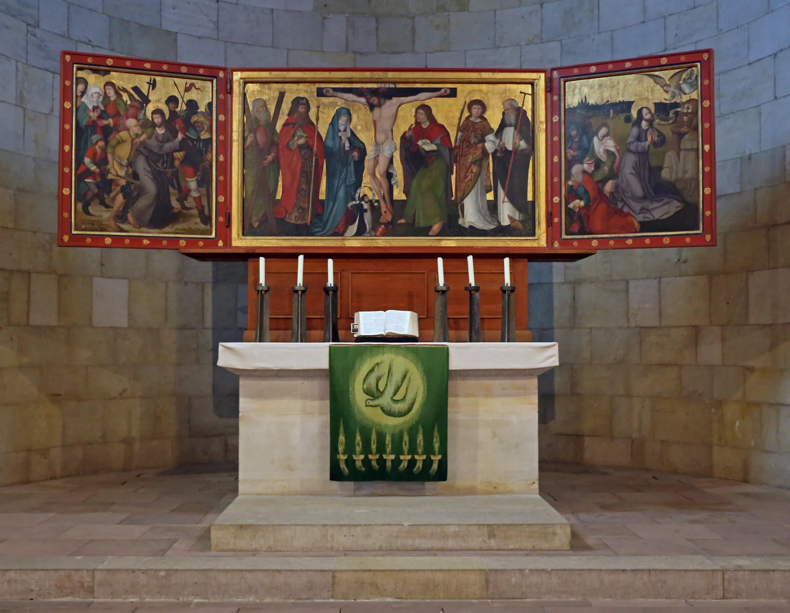 A painted winged altarpiece above a stone altar with candles and a green hanging in St Servatius.