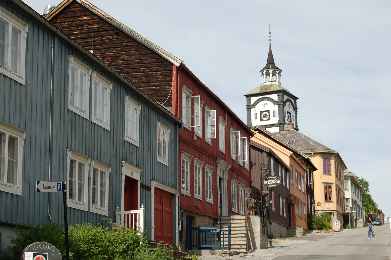 Blue-gray and red wooden houses on Kjerkgata below Røros Church's clock tower.