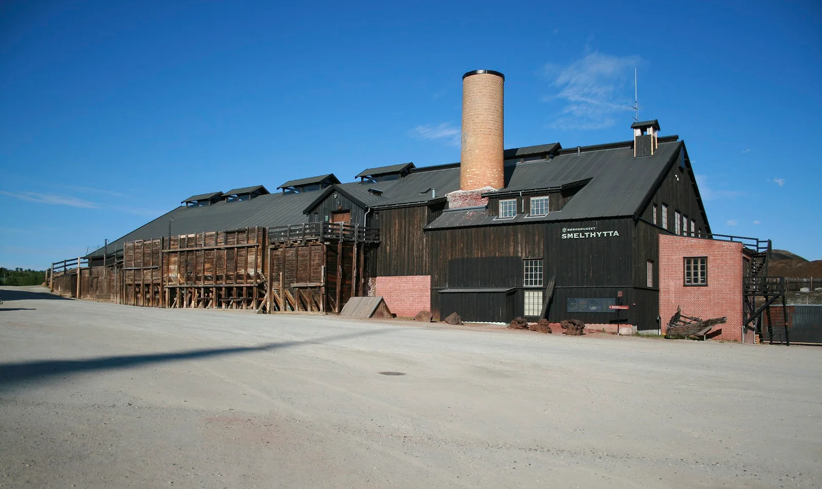 Smelthytta's timber façade and brick chimney face an open gravel forecourt.